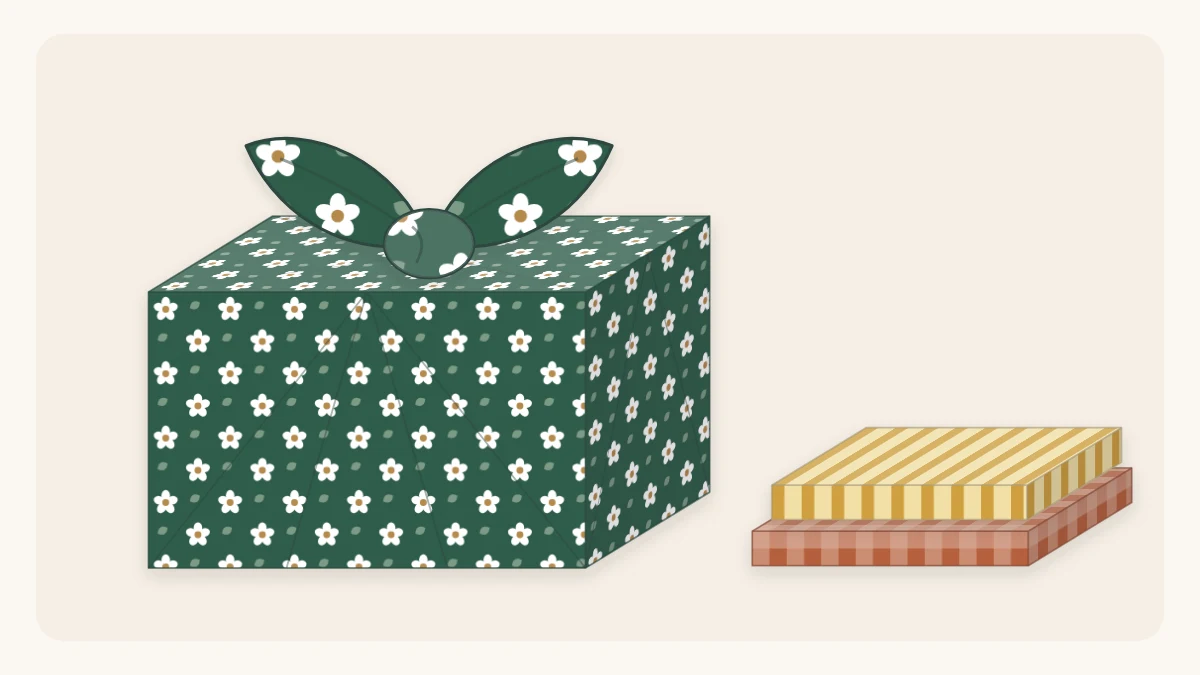 A box wrapped in patterned cloth with corners knotted on top beside two folded fabric squares